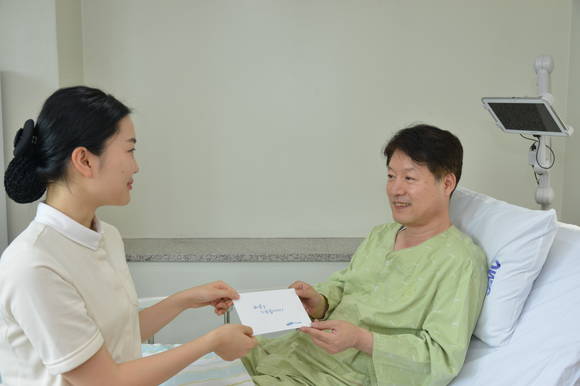 담당 간호사가 환자에게 쾌유 기원 카드를 전달 하고 있다.