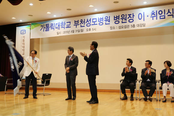 권순석 제17대 가톨릭대학교 부천성모병원장이 제16대 백민우 병원장과 강무일 가톨릭중앙의료원장으로부터 병원기를 전달받아 힘차게 흔들고 있다.