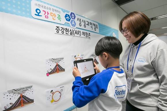 자원 봉사자(사이언스 버디)로 참여한 ㈜한국로슈 직원이 참가 어린이와 함께 증강현실을 체험하고 있다.